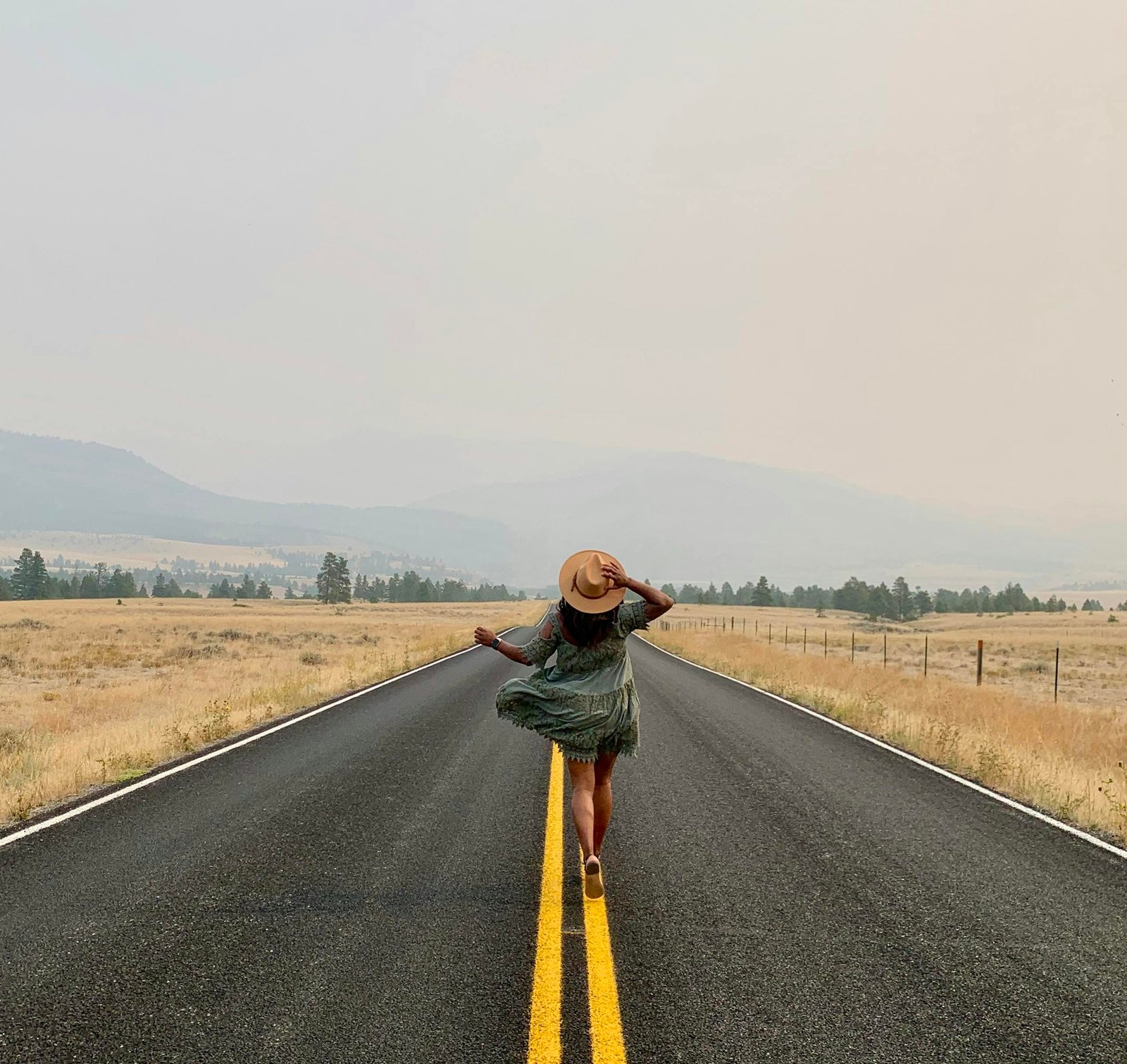 A woman in a dress with a hat walks on a deserted country road in Helena, MT, USA, exuding wanderlust.