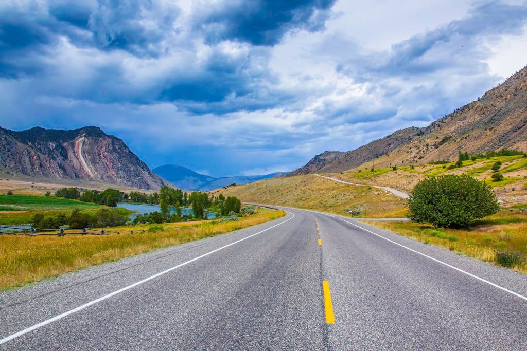 Explore the scenic mountain highway in Montana with vibrant natural beauty under dramatic skies.