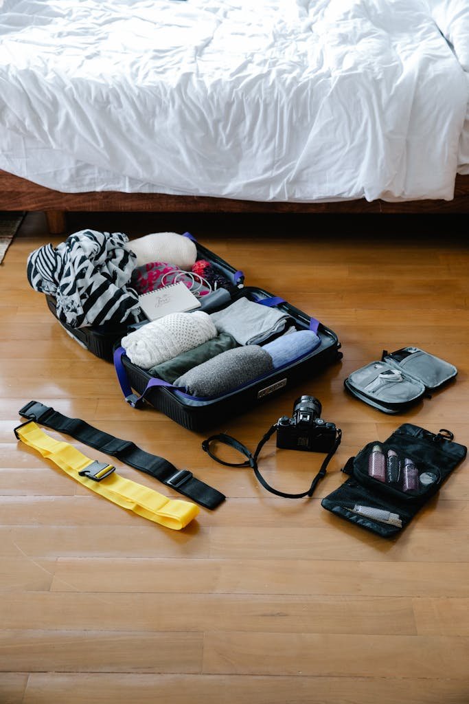 Open suitcase with clothes, camera, and travel essentials neatly arranged on a wooden floor.
