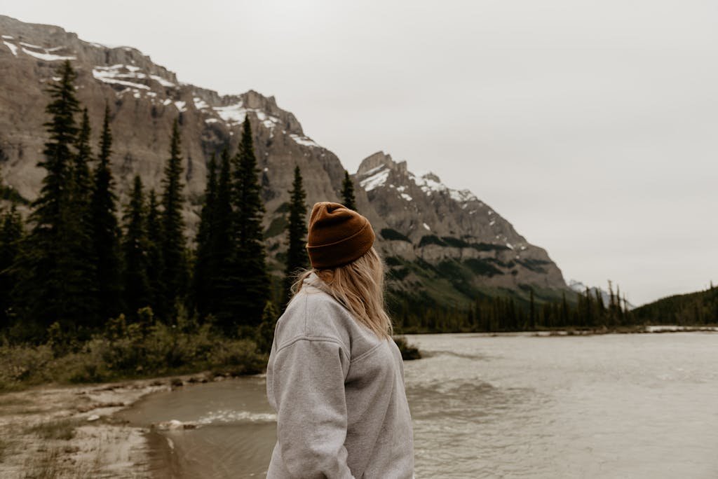 Woman in warm clothing gazing at mountain landscape by a river.